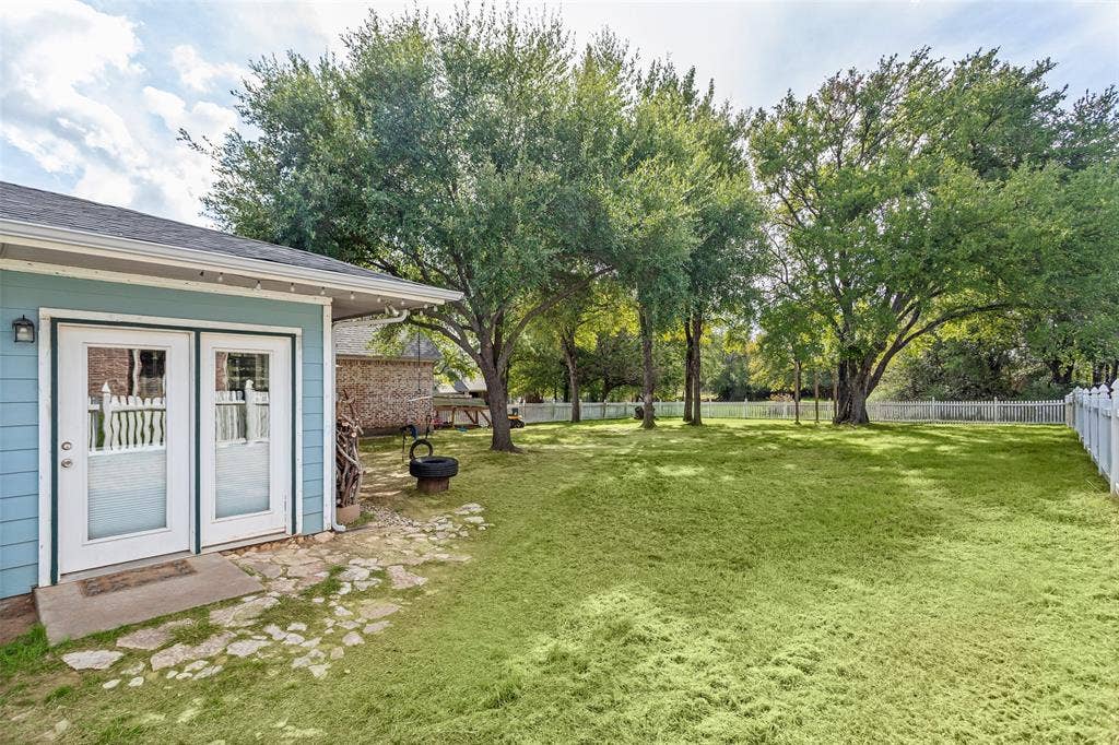 Backyard featuring a manicured lawn, irregular flagstone paving, white vinyl fencing, and mature trees