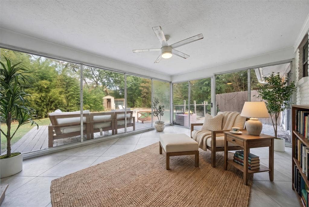 605 Ranier Circle, Garland, TX 75041 Enclosed sunroom featuring expansive glass walls, large-format tile flooring, a central ceiling fan, and built-in shelving