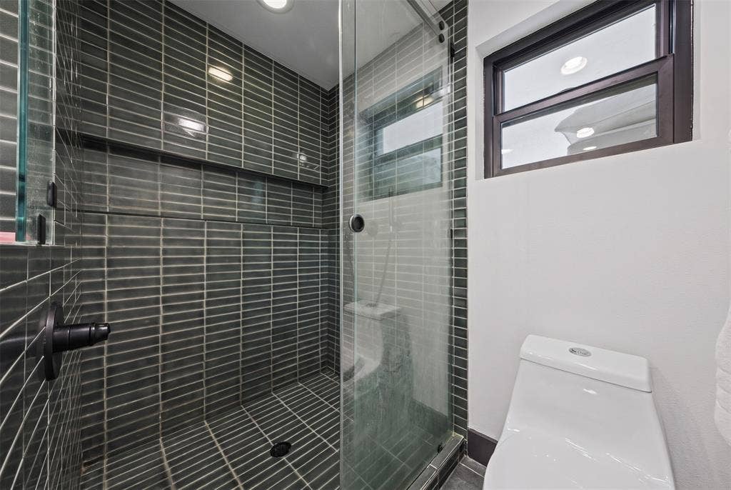 605 Ranier Circle, Garland, TX 75041 Walk-in shower featuring dark grey vertical tile surround, recessed wall niche, frameless glass enclosure, and black hardware, complemented by a dual-flush toilet
