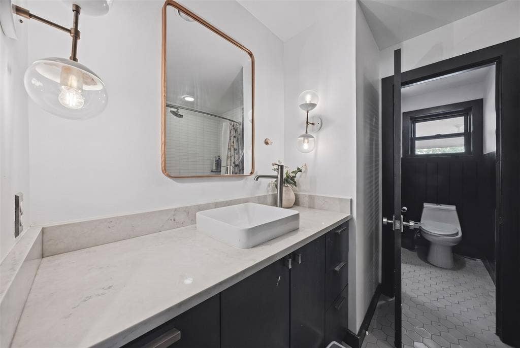 605 Ranier Circle, Garland, TX 75041 Modern vanity with a light-toned solid surface countertop and rectangular vessel sink, paired with a copper-trimmed mirror, glass globe wall lighting, and hexagonal tile flooring