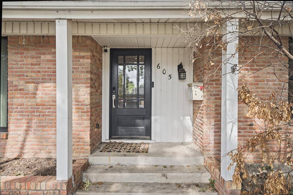 605 Ranier Circle, Garland, TX 75041 Covered front entryway featuring a masonry brick facade, vertical paneling, a multi-pane glass-inlay door, and an attached exterior light fixture
