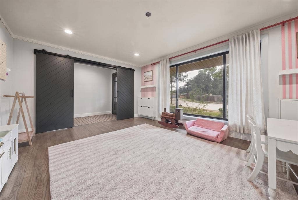 605 Ranier Circle, Garland, TX 75041 Interior space featuring wood-finish flooring, large picture window with track-mounted drapery, and dual matte black chevron-pattern sliding barn doors