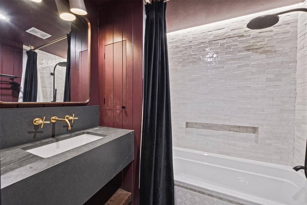 605 Ranier Circle, Garland, TX 75041 Floating vanity featuring a matte-finish dark countertop and integrated rectangular sink, accented by metallic wall-mounted widespread faucets, a textured white tile shower surround with a built-in recessed niche, and a metallic-framed vanity mirror