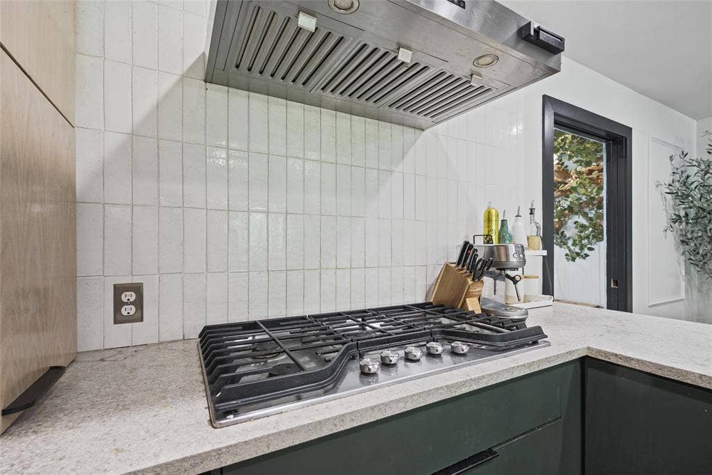 605 Ranier Circle, Garland, TX 75041 Stainless steel gas cooktop with a professional-grade range hood, vertical white subway tile backsplash, solid-surface countertops, and dark-toned cabinetry