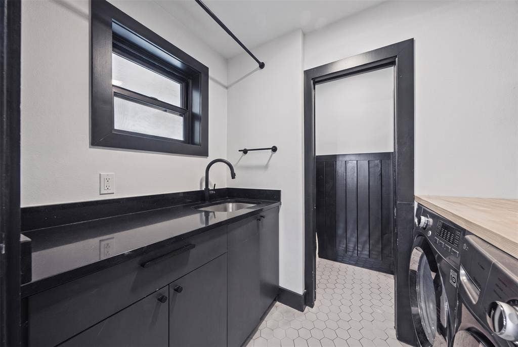 605 Ranier Circle, Garland, TX 75041 Laundry space featuring matte black cabinetry, dark stone-finish countertops, stainless steel undermount sink with a matte black faucet, hexagonal floor tiling, and black-trimmed woodwork
