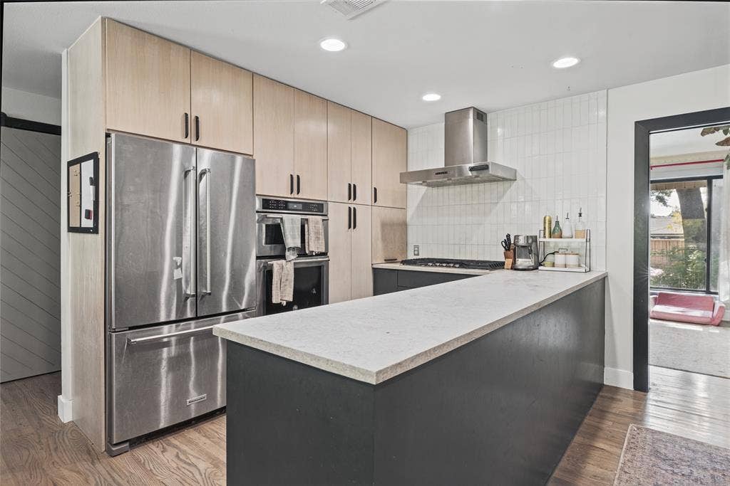 605 Ranier Circle, Garland, TX 75041 Kitchen featuring light-finish cabinetry, stainless steel appliances, a solid-surface breakfast bar, subway-tiled backsplash, and wood-finish flooring