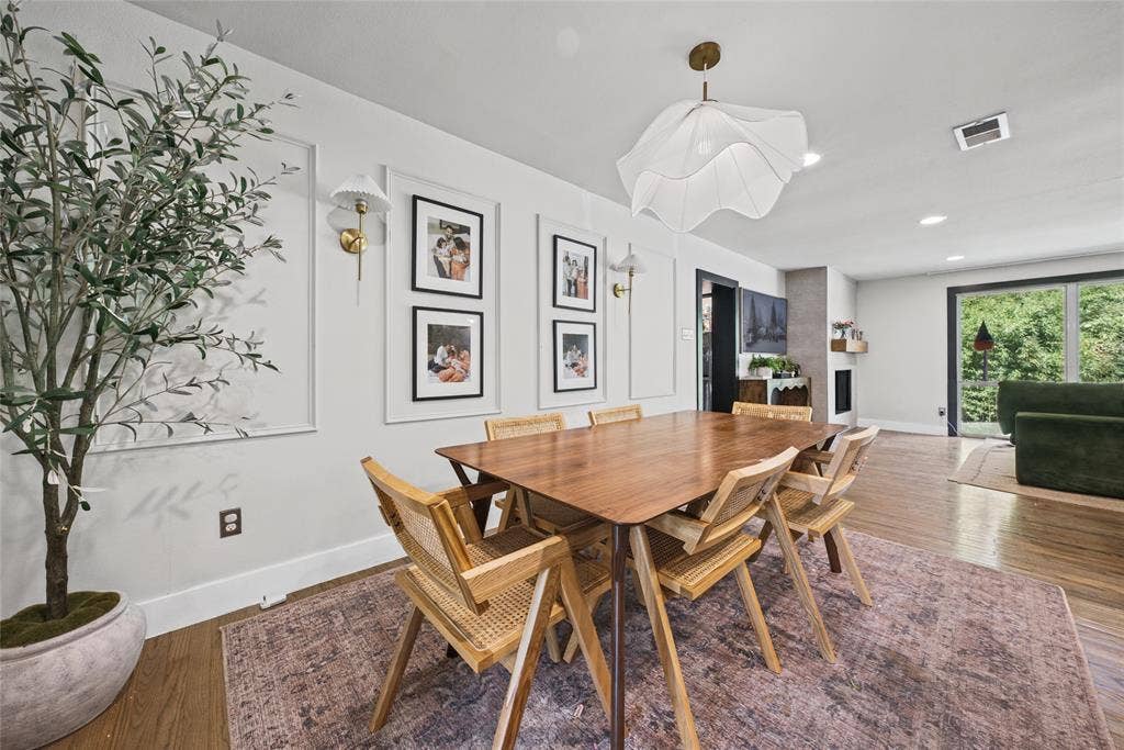 605 Ranier Circle, Garland, TX 75041 Dining area featuring wall molding panels, decorative brass wall sconces, a contemporary pendant light, wood-finish flooring, and a fireplace with a textured surround