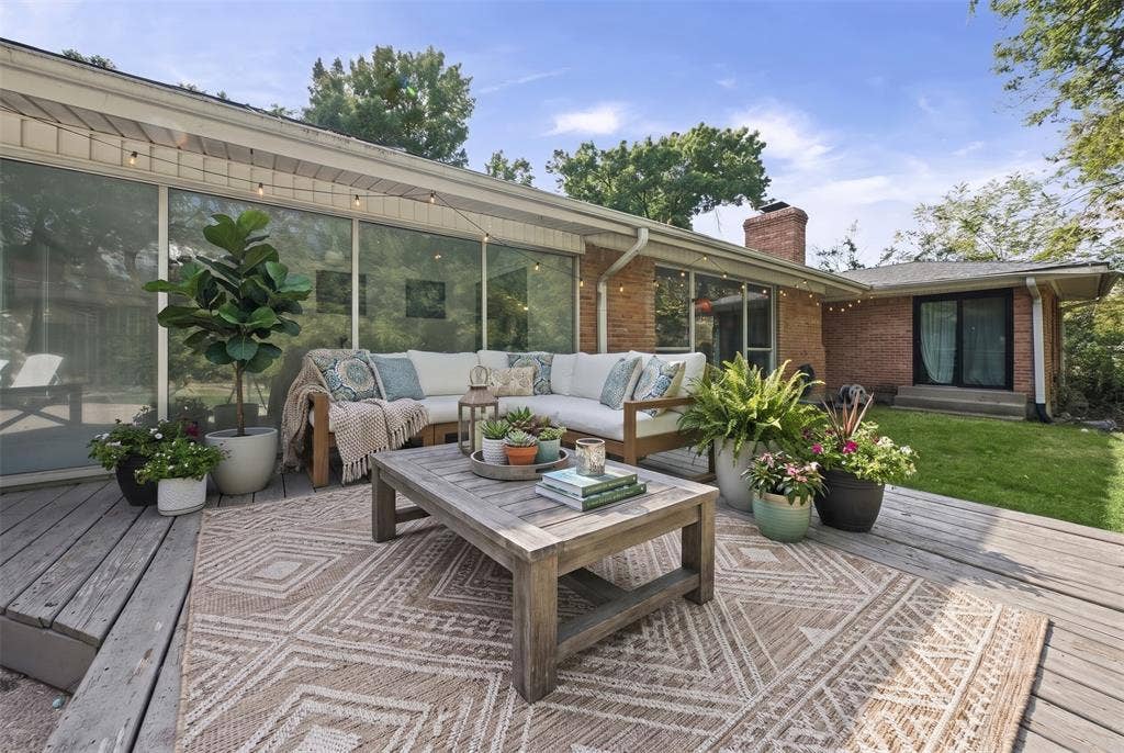 605 Ranier Circle, Garland, TX 75041 Spacious wood deck featuring floor-to-ceiling glass paneling, exposed brick exterior cladding, a brick chimney, and a landscaped lawn area