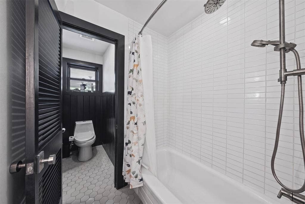 605 Ranier Circle, Garland, TX 75041 Bathroom featuring white vertical tile shower surround, chrome multi-function shower fixture, hexagonal floor tile, and black louvered door