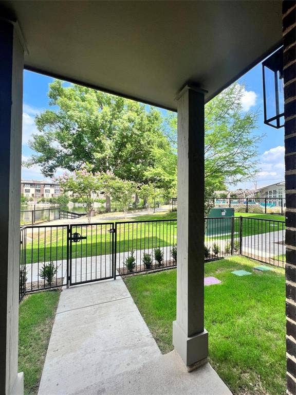 4020 McEwen Road, #4103, Farmers Branch, TX 75244 Covered porch featuring a concrete patio, brick exterior wall, and metal light fixture, opening to a fenced yard with a concrete walkway and manicured lawn