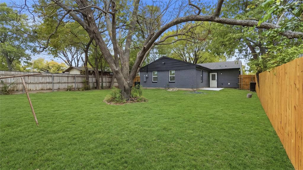 4330 Scottsdale Drive, Mesquite, TX 75150 Expansive backyard featuring a manicured lawn, mature trees, wood privacy fencing, and a concrete patio
