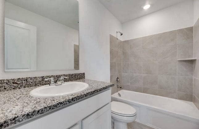 Bathroom featuring a vanity with a stone-finish countertop, an integrated oval sink, a wall-mounted mirror, and a tub-shower combination with floor-to-ceiling tile surround