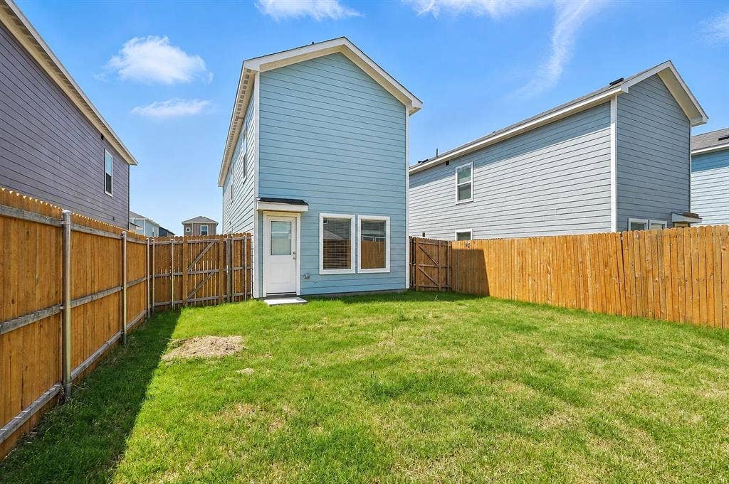 Rear exterior featuring light blue horizontal lap siding, white window trim, and a fully enclosed wood fence surrounding a grass yard