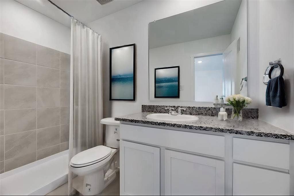 Bathroom featuring a vanity with shaker-style white cabinetry, stone-finish countertop, integrated basin, and a large wall-mounted mirror
