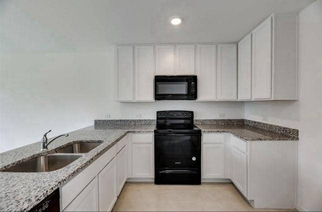 Kitchen featuring white cabinetry, stone-surface countertops, dual-basin stainless steel sink with high-arc faucet, and black built-in appliances