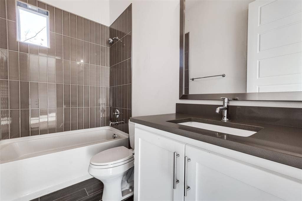 Bathroom featuring a white vanity cabinet with a dark countertop, integrated sink, vertical tile surround in the shower area, and a large wall-mounted mirror
