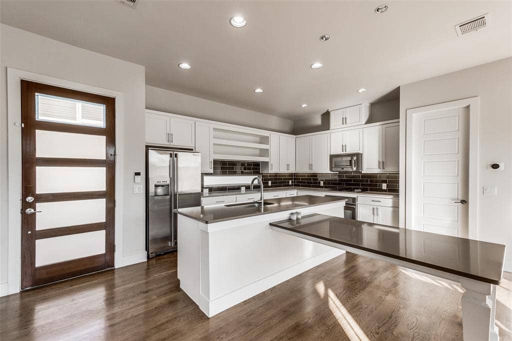 Kitchen featuring white cabinetry, an island with an extended countertop, stainless steel appliances, dark subway tile backsplash, and wood-finish flooring