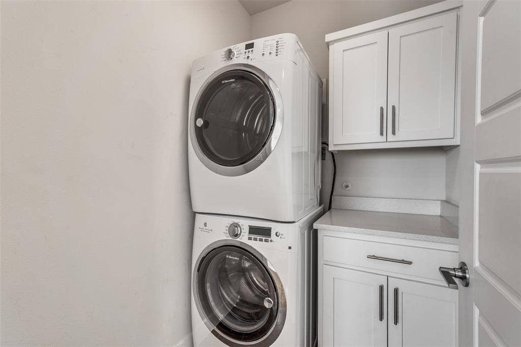 Laundry area featuring a stackable washer and dryer, white shaker-style cabinetry, and solid surface countertop