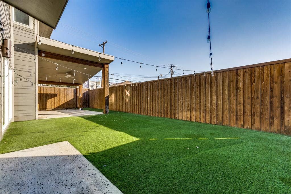 Backyard featuring a covered patio with a ceiling fan, synthetic turf lawn, and a privacy wood fence