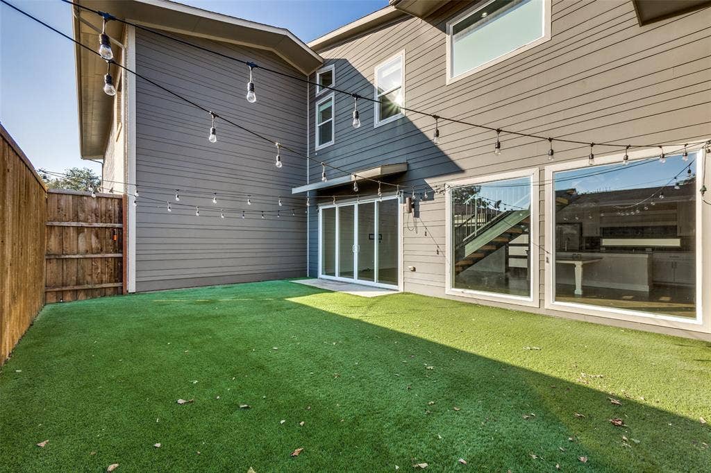 Private backyard featuring low-maintenance synthetic turf, horizontal lap siding, and large-format glass paneled doors