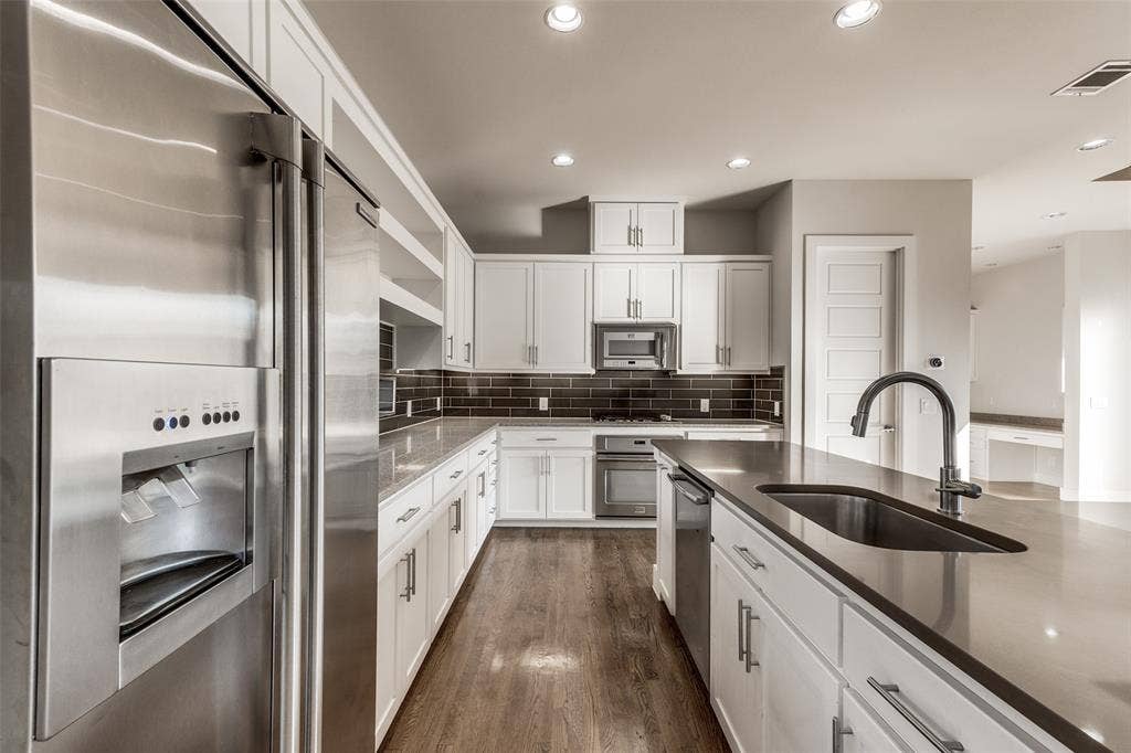 Kitchen featuring white cabinetry, stainless steel appliances, dark tile backsplash, neutral countertops, and wood-finish flooring
