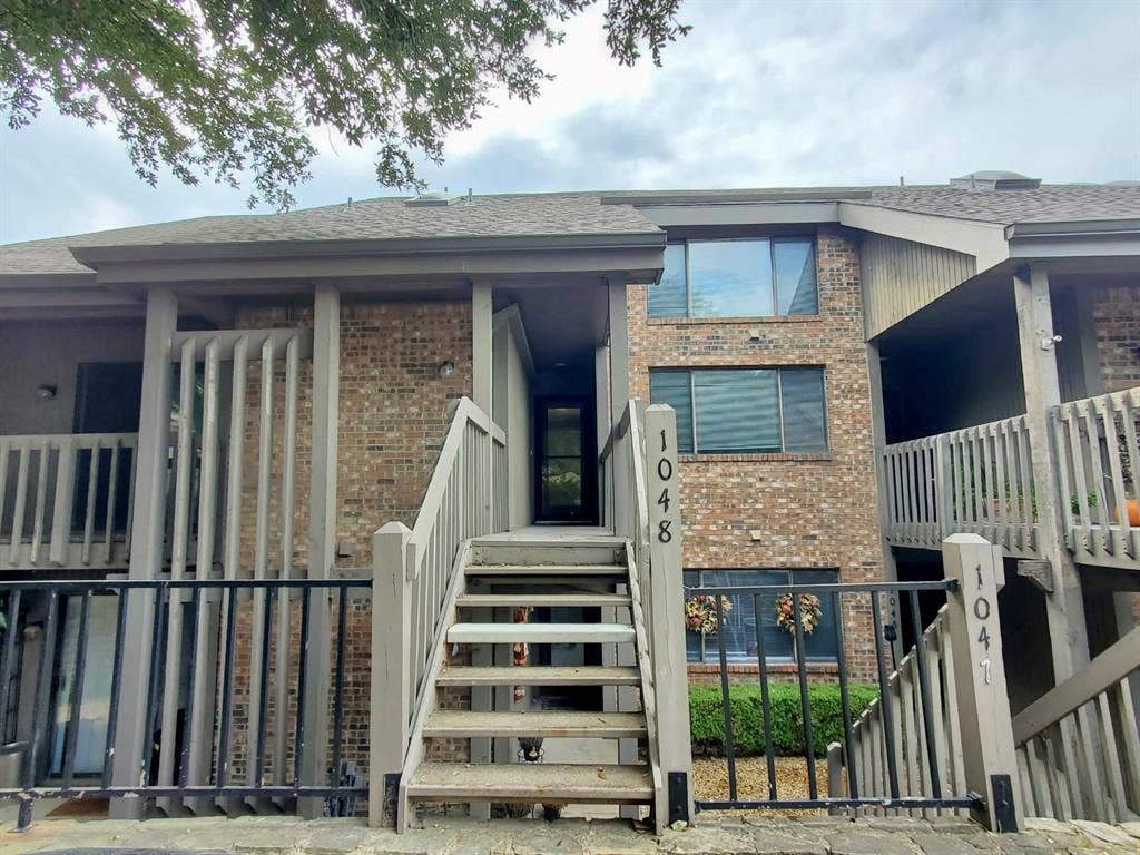 Multi-level exterior featuring brick masonry, timber-style accents, private staircases with railings, and neutral-toned shingle roofing