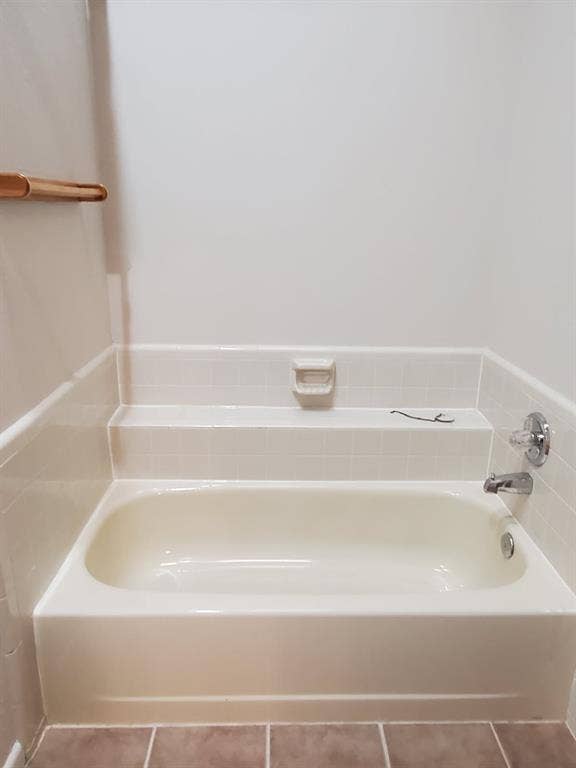 Bathtub featuring integrated tile surround, built-in soap dish, chrome fixtures, and stone-finish floor tile