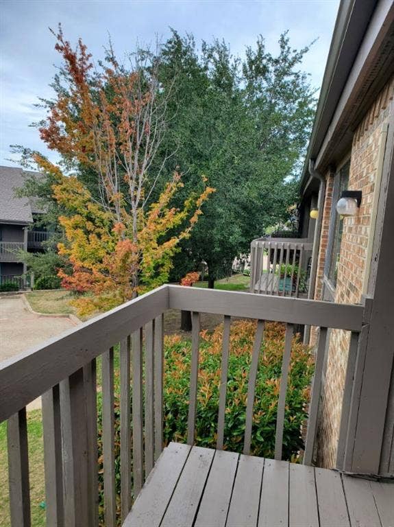 Covered balcony featuring wood-slat decking, a painted wooden railing, and an attached exterior wall-mounted light fixture