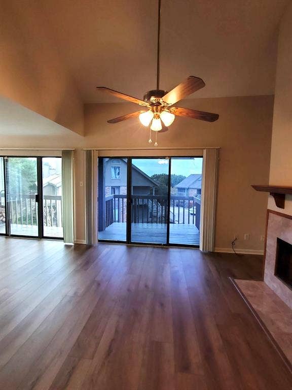 Vaulted ceilings, wood-finish flooring, dual sliding glass doors, fireplace with tiled surround, and ceiling fan with integrated light fixture