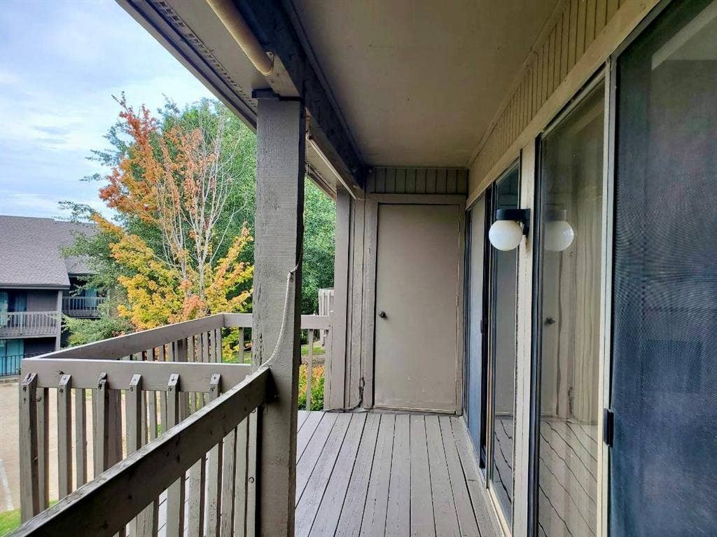 Covered outdoor balcony featuring wood-slat flooring, vertical wood railings, a dedicated exterior storage closet, and a mounted globe-style sconce