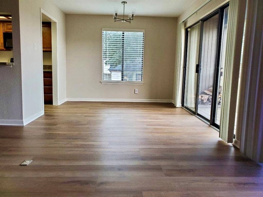 Wood-finish flooring, sliding glass patio door, multi-arm chandelier, and neutral wall color