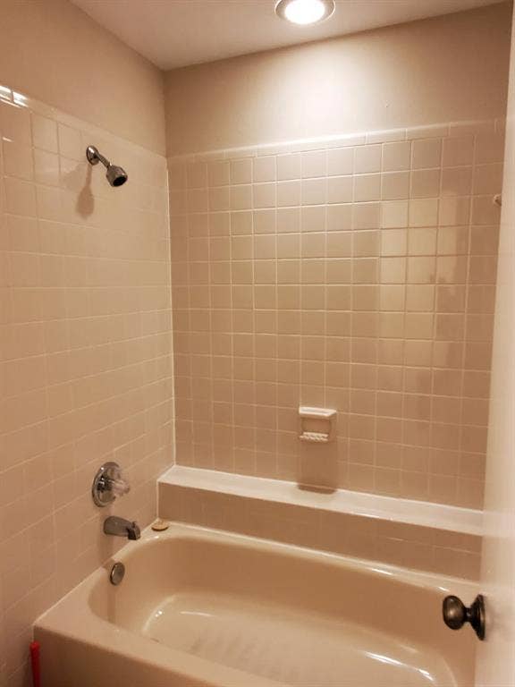 Bathtub with an integrated shower, chrome fixtures, built-in soap dish, and ceramic tile surround