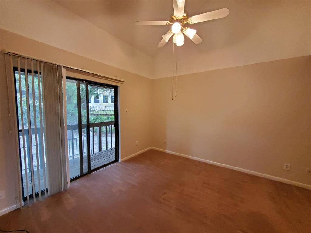 Vaulted ceilings, wood-finish flooring, ceiling fan with multi-light fixture, and sliding glass doors opening to an exterior deck