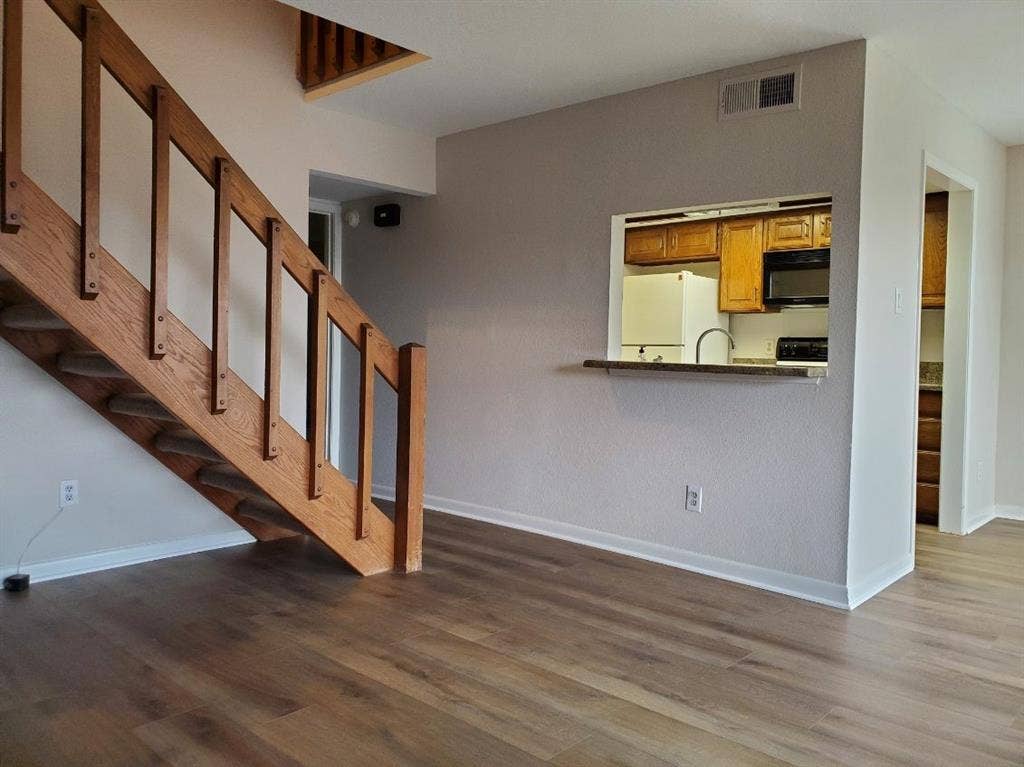 Wood-finish flooring throughout, wooden staircase with open-rail design, and kitchen pass-through window with a solid surface ledge