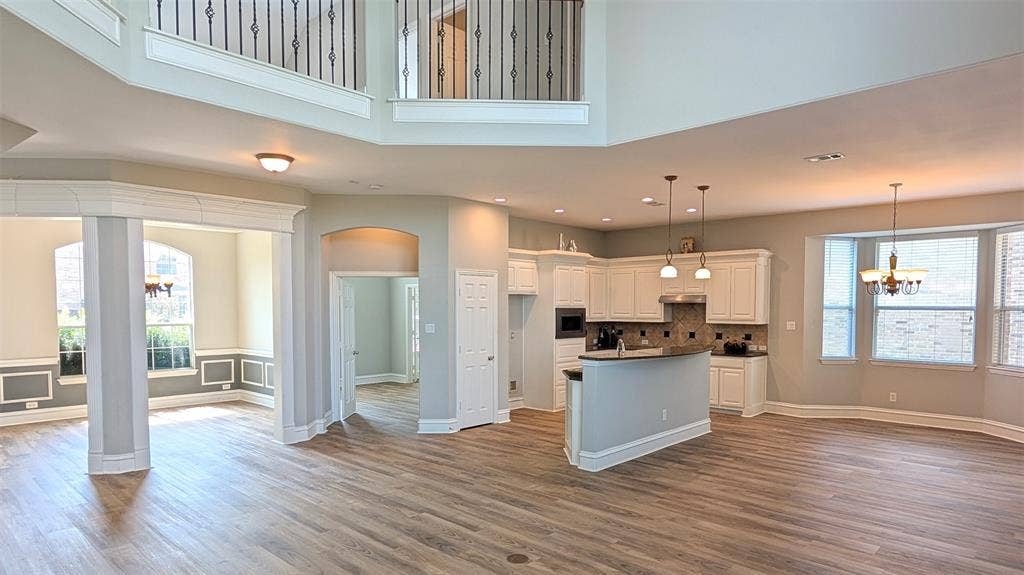 4221 Crestfield Drive, Richardson, TX 75082 Open-concept interior featuring wood-finish flooring, a two-story ceiling with a decorative mezzanine railing, white cabinetry, a peninsula island, and arched architectural detailing