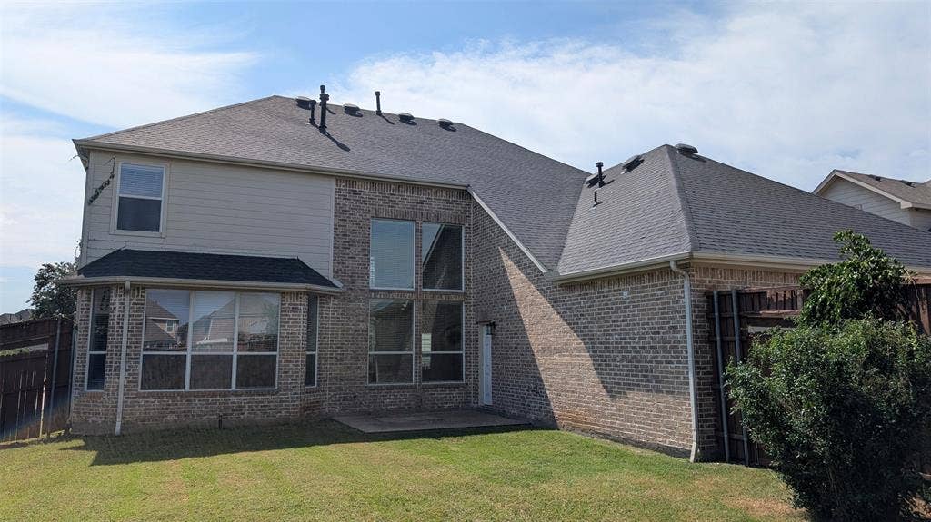 4221 Crestfield Drive, Richardson, TX 75082 Exterior rear elevation featuring brick and horizontal siding, asphalt shingle roof, two-story window configurations, and a concrete patio