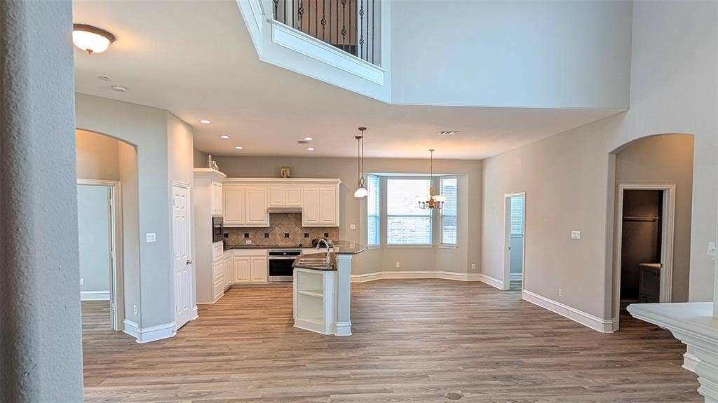 4221 Crestfield Drive, Richardson, TX 75082 Open-concept kitchen featuring white cabinetry, wood-finish flooring, a center island with sink, and double-height ceilings with an overlook