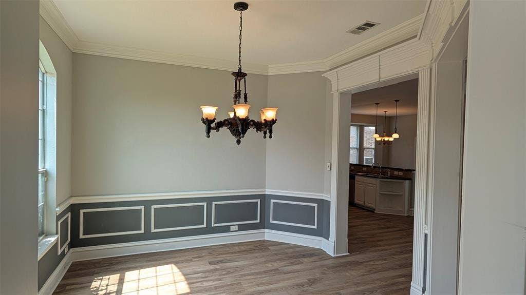 4221 Crestfield Drive, Richardson, TX 75082 Interior space featuring wood-finish flooring, two-toned walls with wainscoting, crown molding, arched window, and a multi-light chandelier