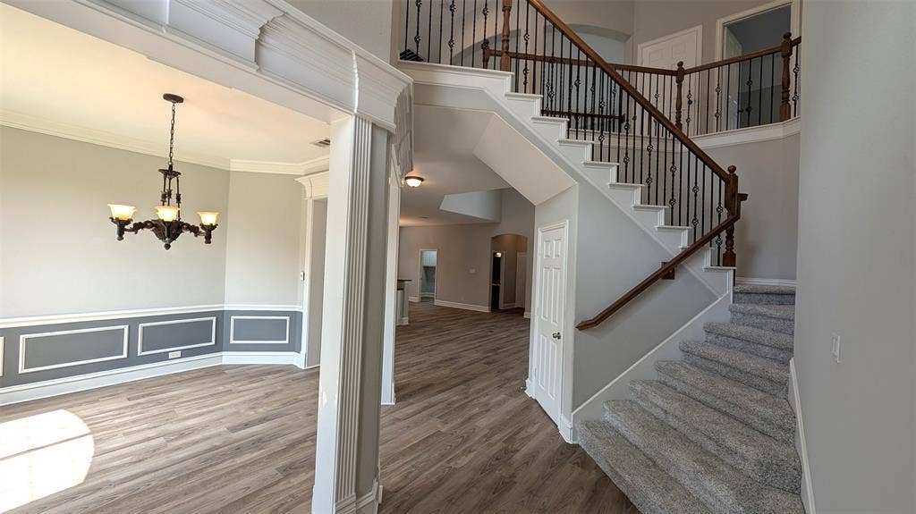 4221 Crestfield Drive, Richardson, TX 75082 Foyer featuring wood-finish flooring, a staircase with decorative metal balusters and wooden handrail, wainscoting, and a multi-arm chandelier