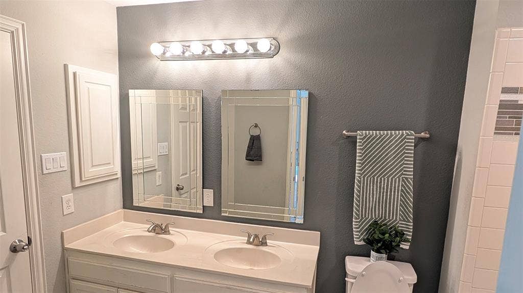 4221 Crestfield Drive, Richardson, TX 75082 Double-sink vanity with a solid-surface countertop, dual rectangular mirrors with beveled edges, and six-bulb vanity lighting