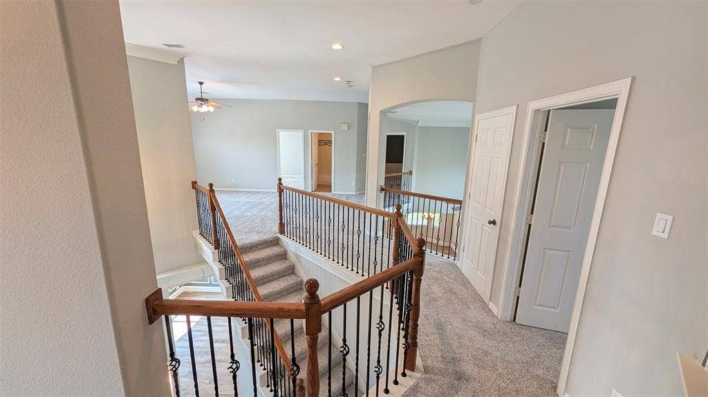 4221 Crestfield Drive, Richardson, TX 75082 Staircase featuring wood handrails, decorative metal balusters, carpeted flooring, and arched architectural detailing