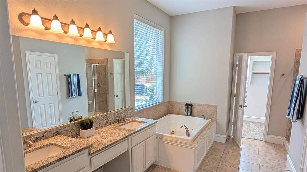 4221 Crestfield Drive, Richardson, TX 75082 Dual-sink vanity with stone-finish countertops, soaking tub with tile surround, large wall-mounted mirror, and tile flooring