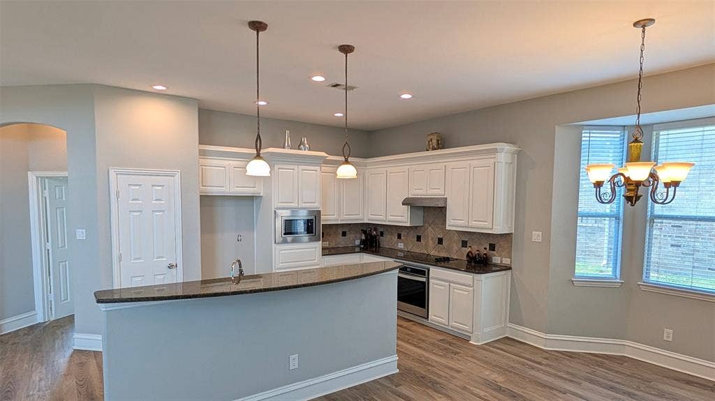 4221 Crestfield Drive, Richardson, TX 75082 Kitchen featuring white shaker-style cabinetry, dark stone countertops, stainless steel appliances, pendant lighting, and wood-finish flooring