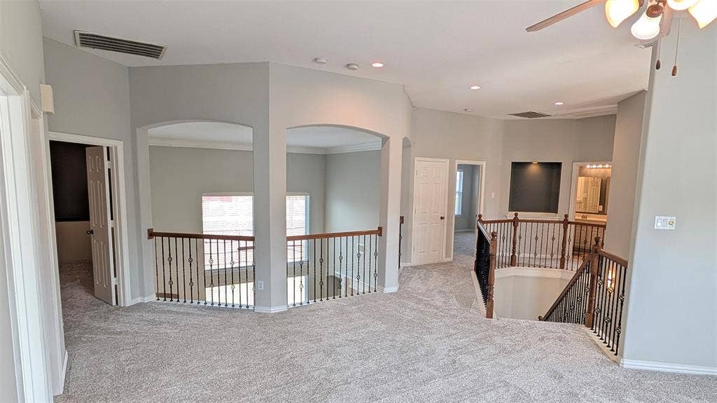4221 Crestfield Drive, Richardson, TX 75082 Open loft area featuring vaulted ceilings, recessed lighting, metal balusters with wooden handrails, arched architectural cutouts, and a built-in recessed niche