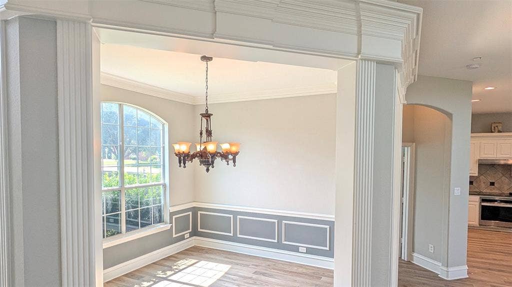4221 Crestfield Drive, Richardson, TX 75082 Arched window with grid detailing, decorative wainscoting, crown molding, fluted column framing, and multi-bulb metal chandelier