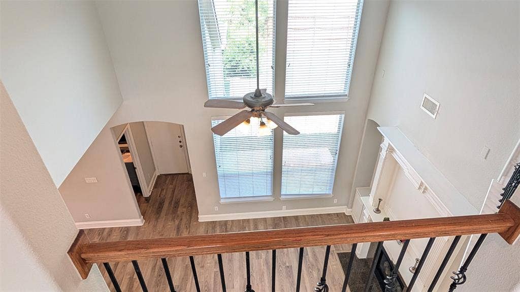 4221 Crestfield Drive, Richardson, TX 75082 Double-height ceiling, floor-to-ceiling windows, built-in fireplace mantle, wood-finish flooring, and staircase with a wood-finished handrail and metal balusters