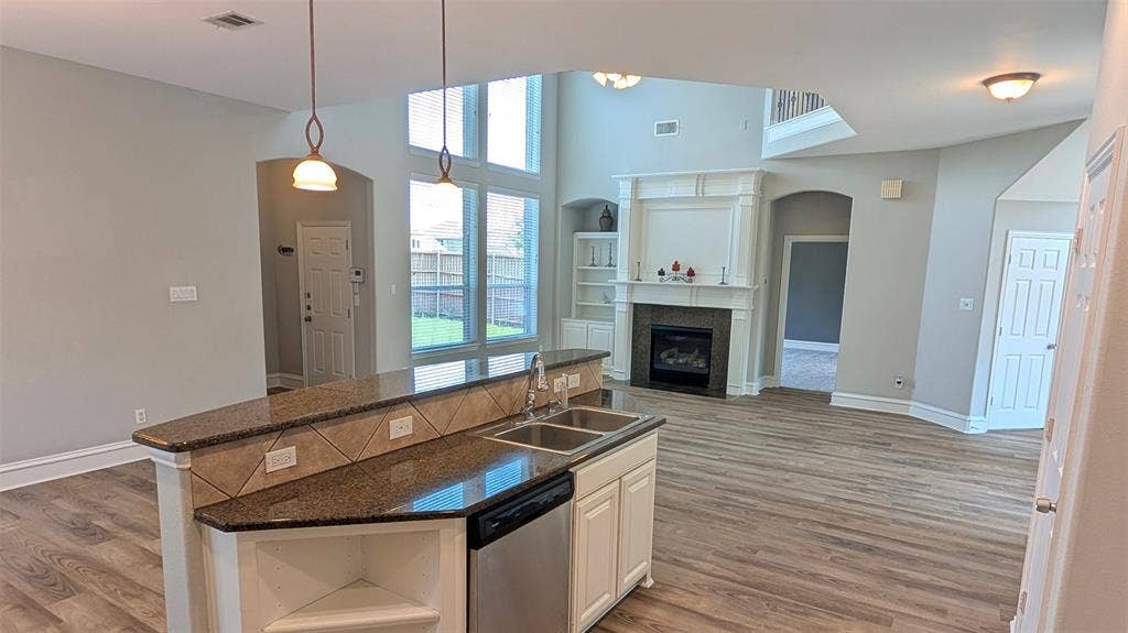 4221 Crestfield Drive, Richardson, TX 75082 Kitchen island with stone countertop and dual-basin stainless steel sink, wood-finish flooring, two-story windows, and fireplace with decorative mantel and built-in shelving