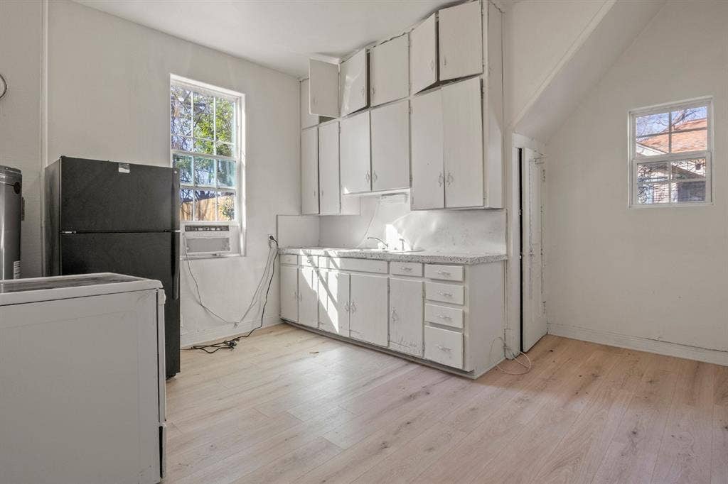 3711 Wendelkin Street, #1, Dallas, TX 75215 Kitchen featuring wood-finish flooring, white cabinetry with extended upper storage, speckled-surface countertops, and dual windows