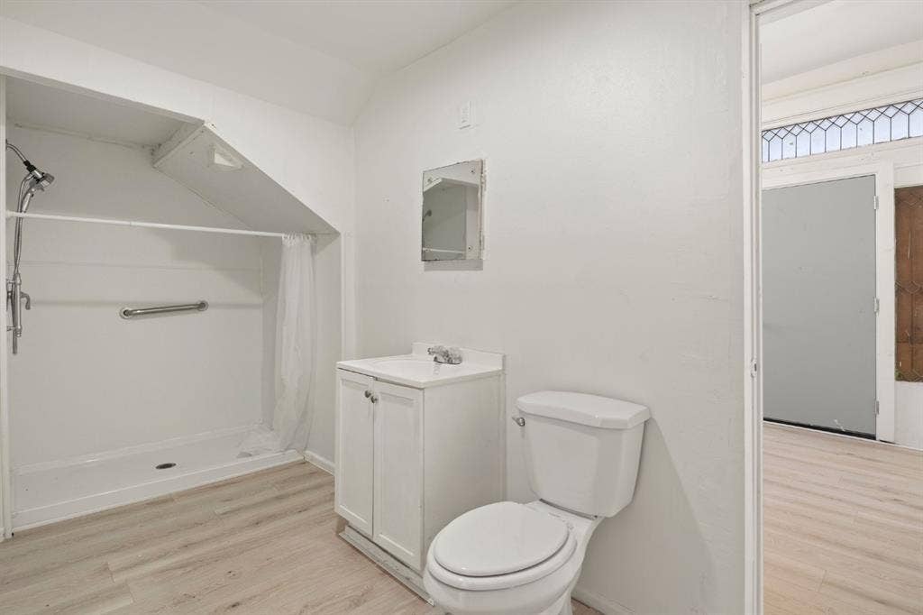 3711 Wendelkin Street, #1, Dallas, TX 75215 Bathroom featuring wood-finish flooring, a white vanity with a single-basin countertop, a wall-mounted medicine cabinet, and a walk-in shower stall with a grab bar