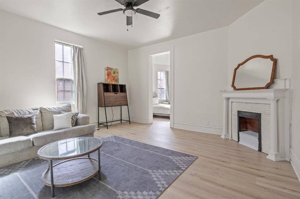 3711 Wendelkin Street, #1, Dallas, TX 75215 Light-filled living area featuring wood-finish flooring, a white mantel fireplace with tile surround, and a ceiling fan